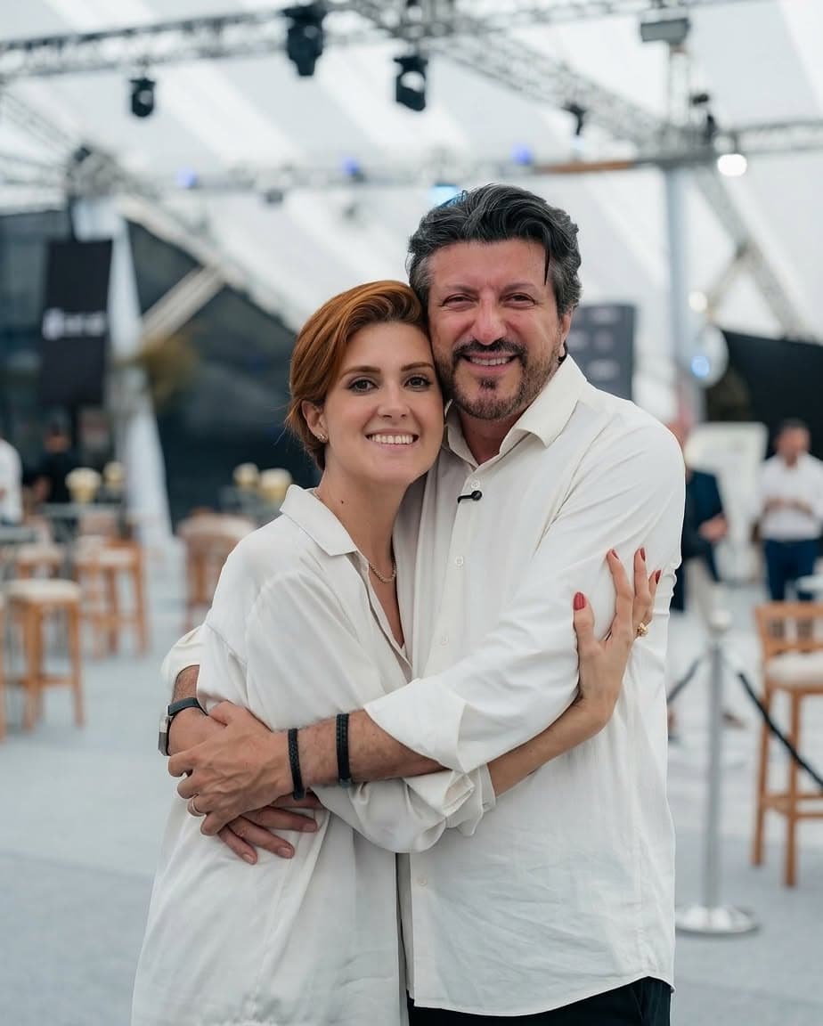 Lito Sousa and his wife Mila Seidl embracing and smiling, both in white shirts, at an outdoor event.
